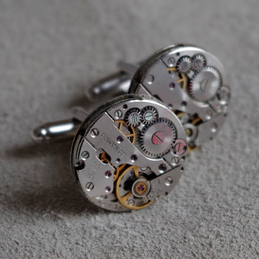A pair of silver cufflinks made from vintage watch mechanisms, featuring intricate gears and jewels.